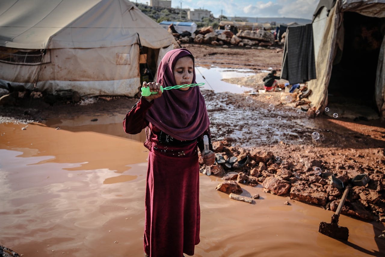 A young girl in Idlib refugee camp blowing bubbles, symbolizing innocence amidst adversity.