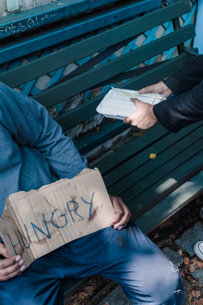 A person helps a homeless individual with food, illustrating kindness and poverty awareness.