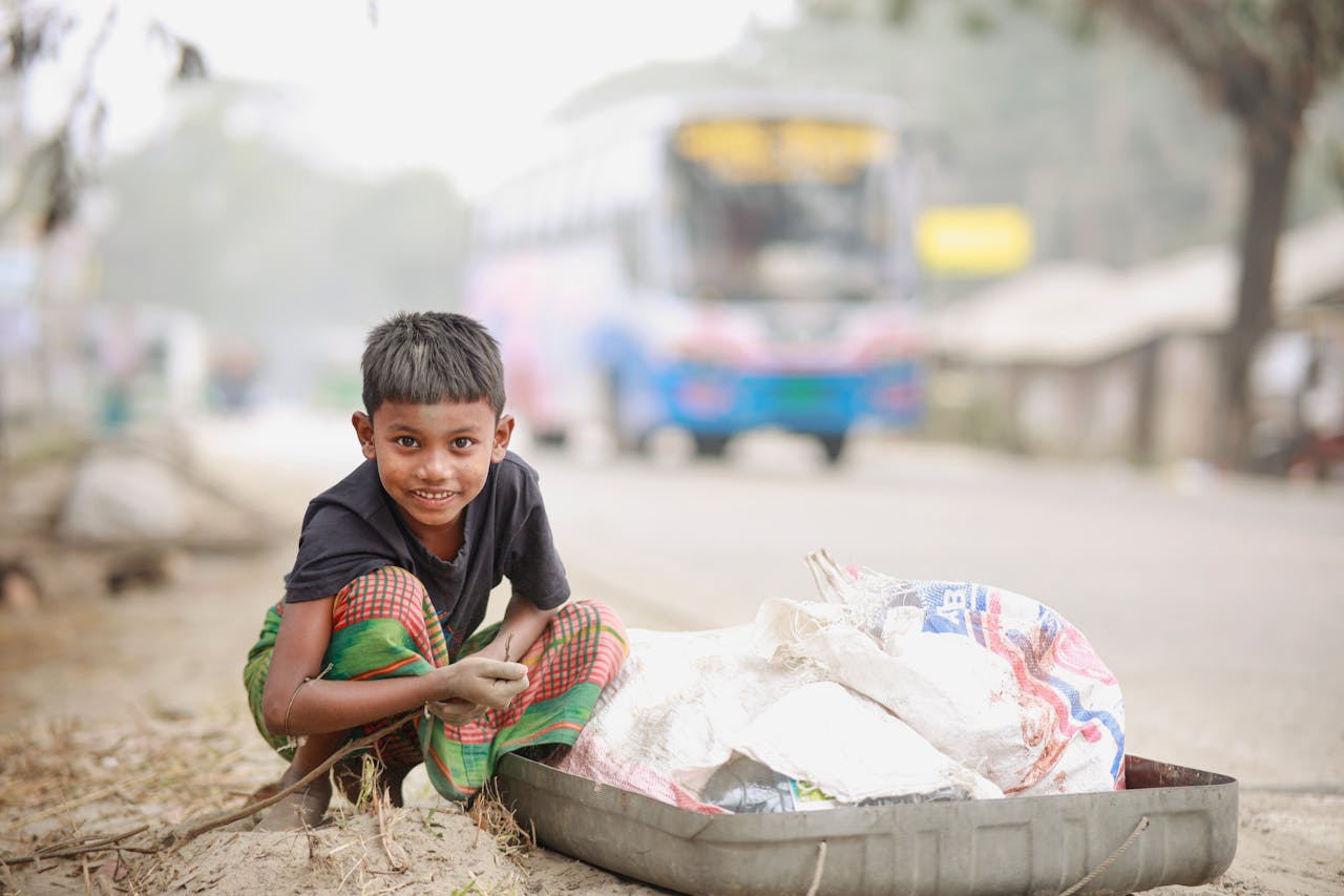 hero-img-02 A cheerful child in traditional clothing gathers recyclable materials on a bustling road.