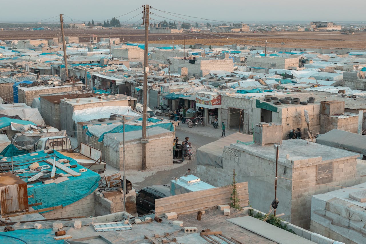 about-01 A broad aerial view of a refugee camp with makeshift shelters and blue tarps in an urban area.
