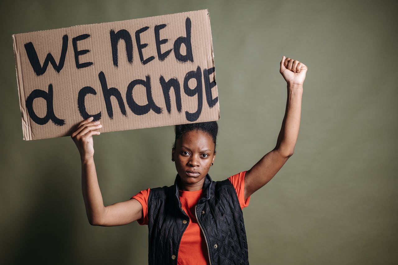 services-01 Black woman advocating for change with a protest sign indoors.